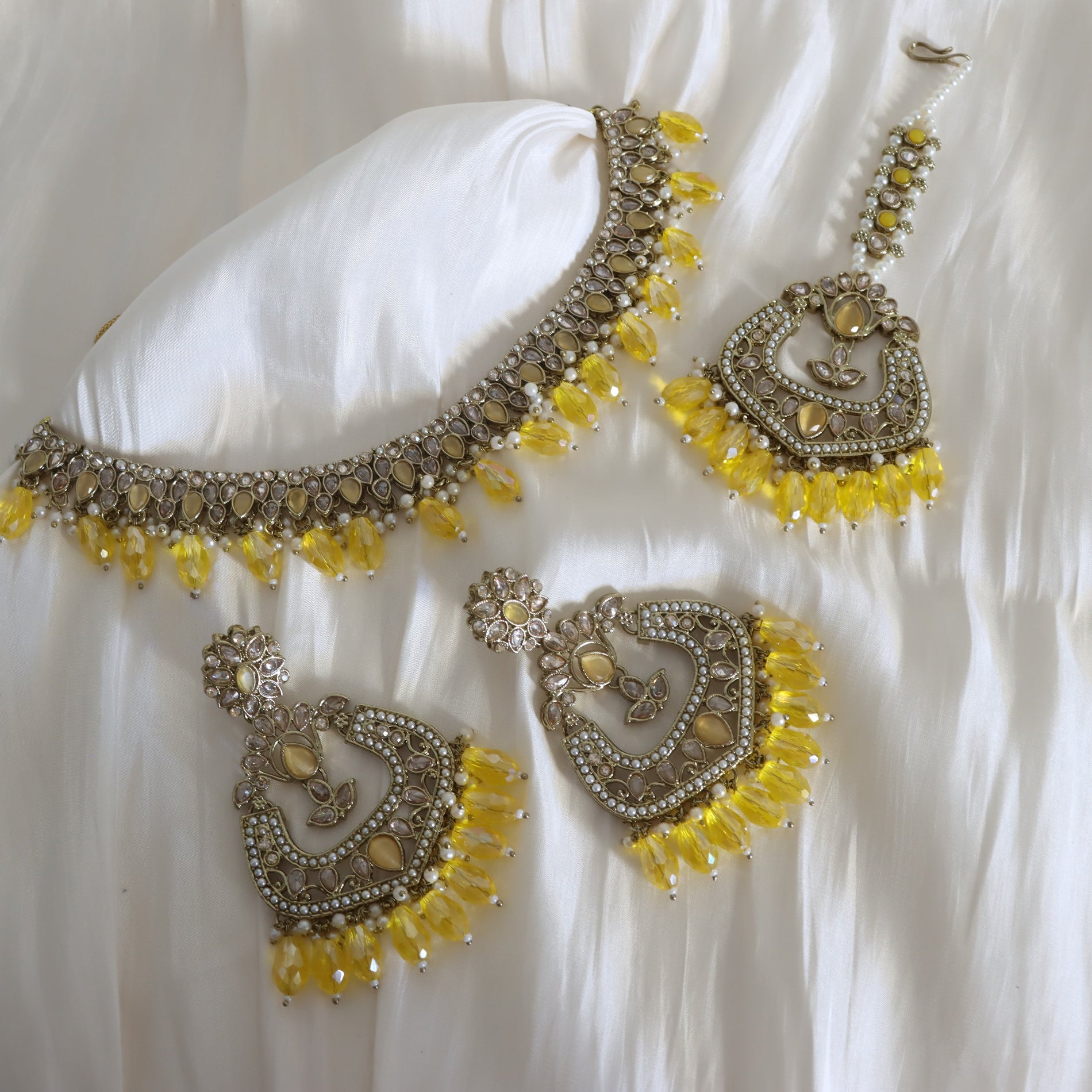 Jewelry set with yellow beads and silver accents on a white fabric background