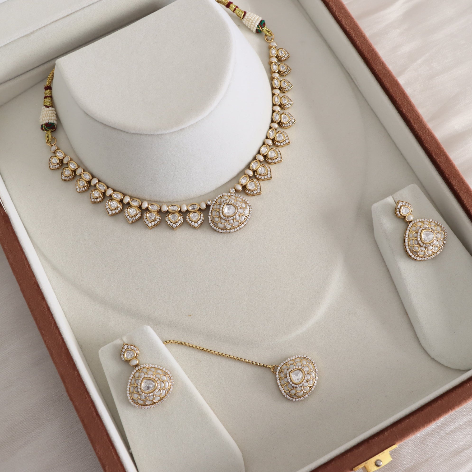 Gold and white stone jewelry set displayed on a white jewelry box, including a necklace on a bust, matching earrings, and a pendant.