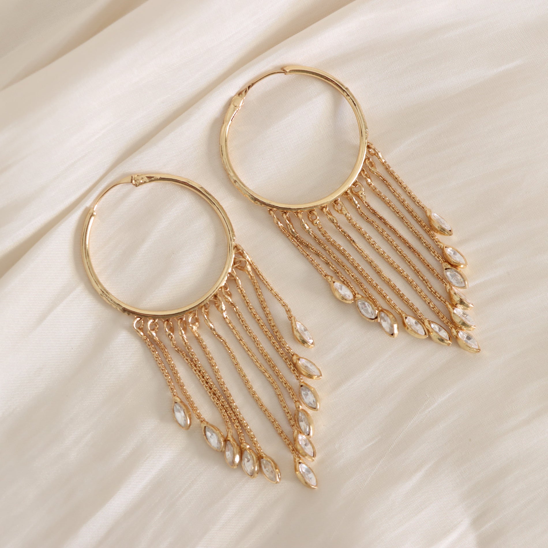 Gold hoop earrings with chain and bead details on a beige fabric background