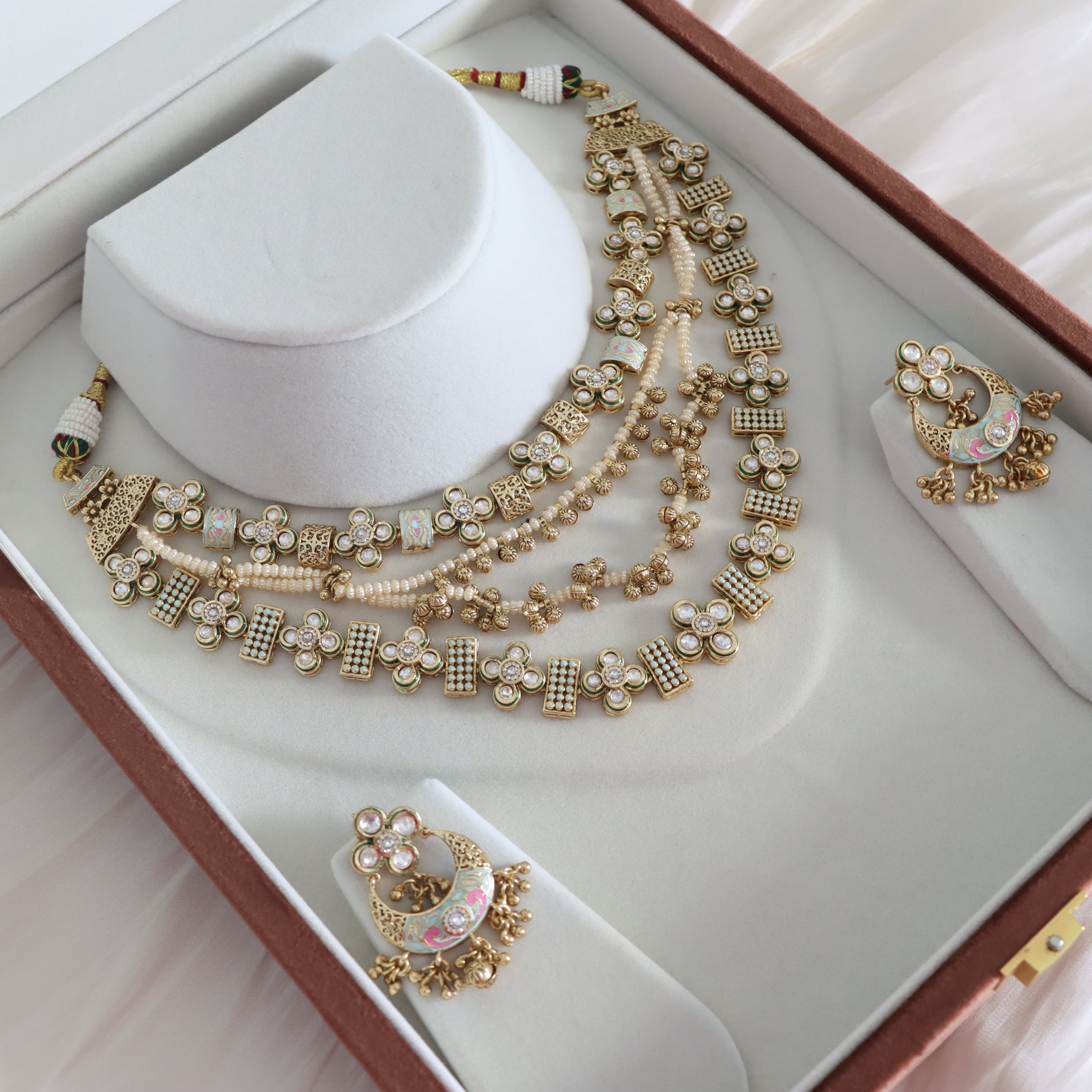 Gold and pearl jewelry set with necklace and earrings on a white stand in a jewelry box.