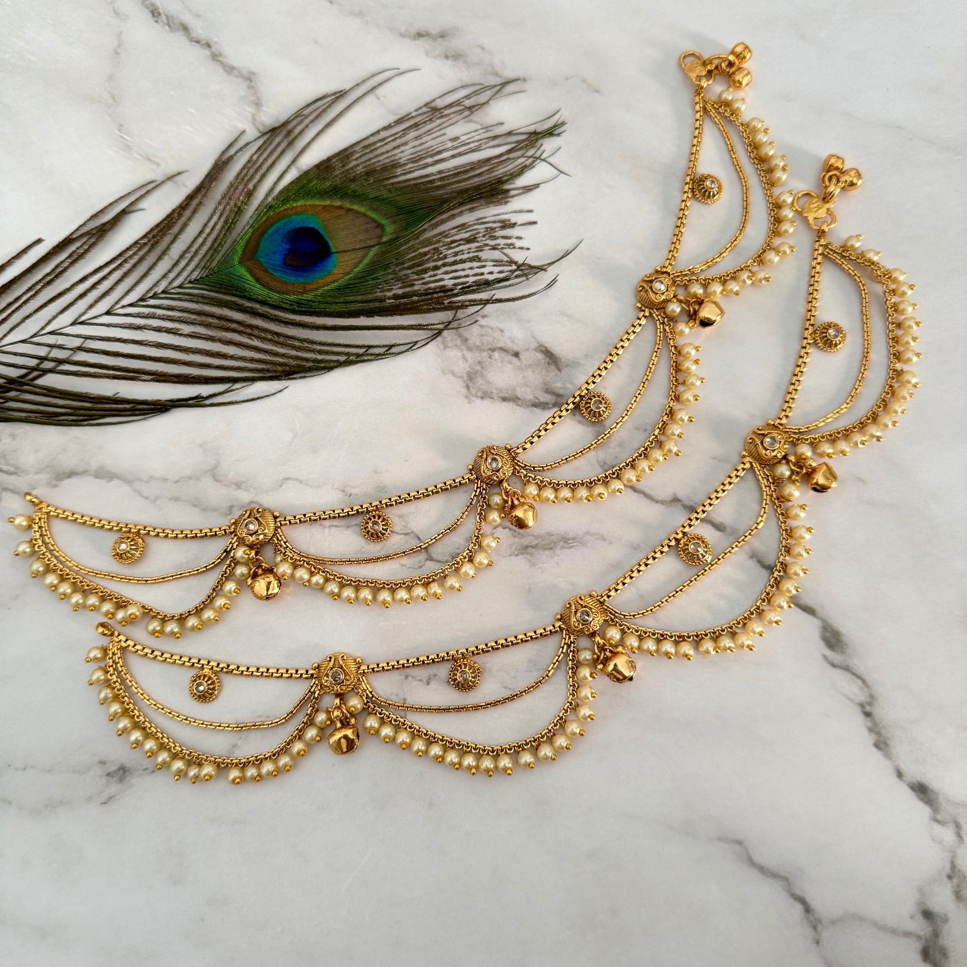 Gold anklet on a marble surface with a peacock feather