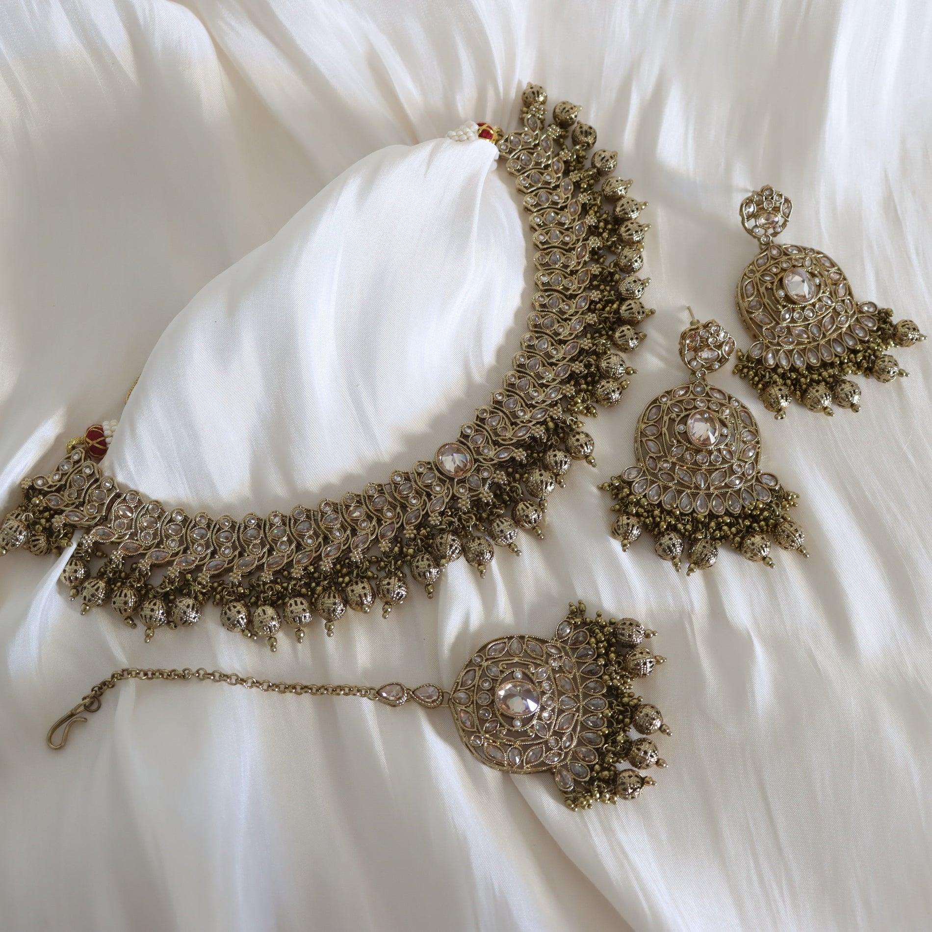 Set of ornate jewelry including a necklace, earrings, and bracelet on a white fabric background.