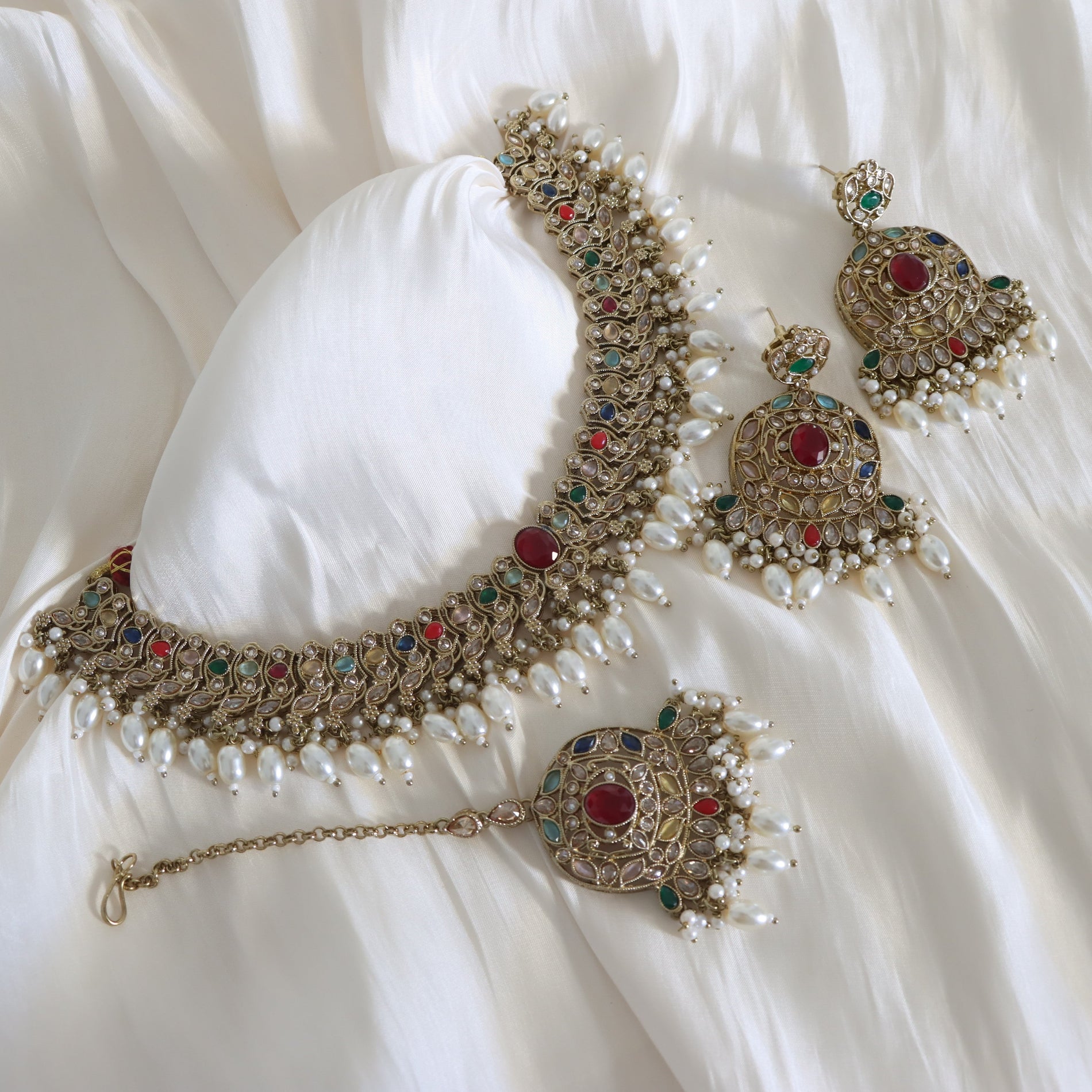 Ornate necklace with red and green gemstones on a white fabric background