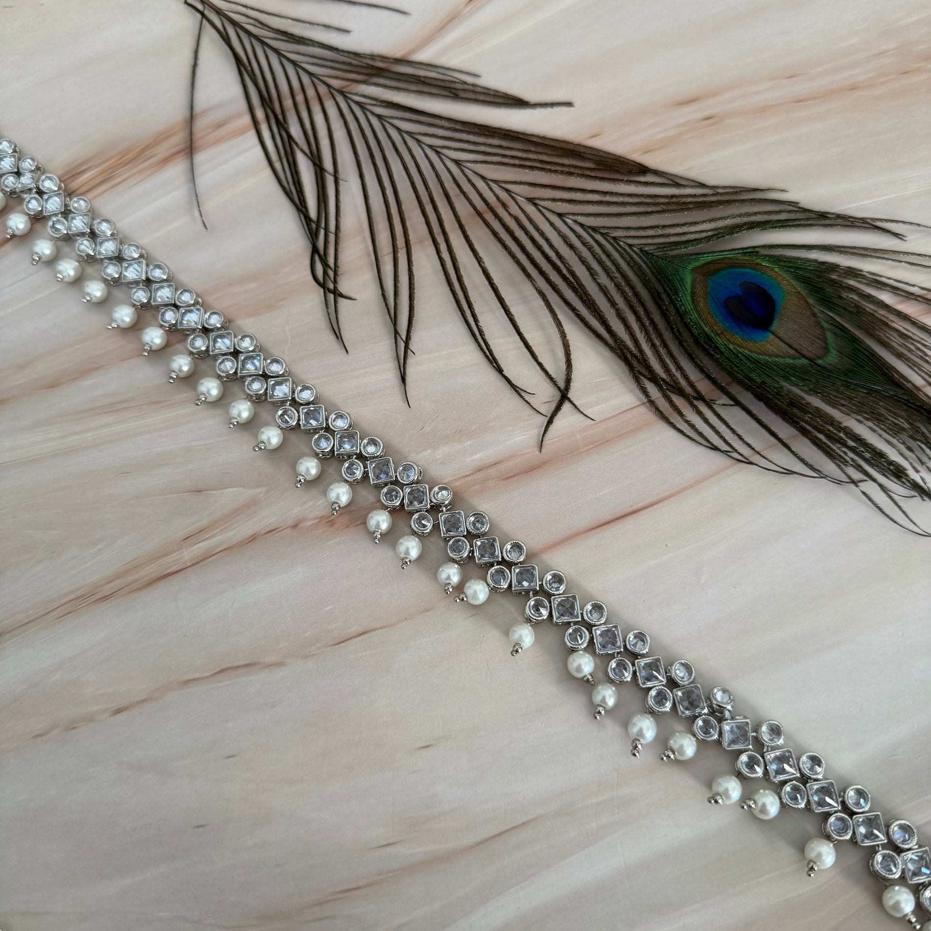 Decorative belt with pearls and crystals on a marble surface with a peacock feather.