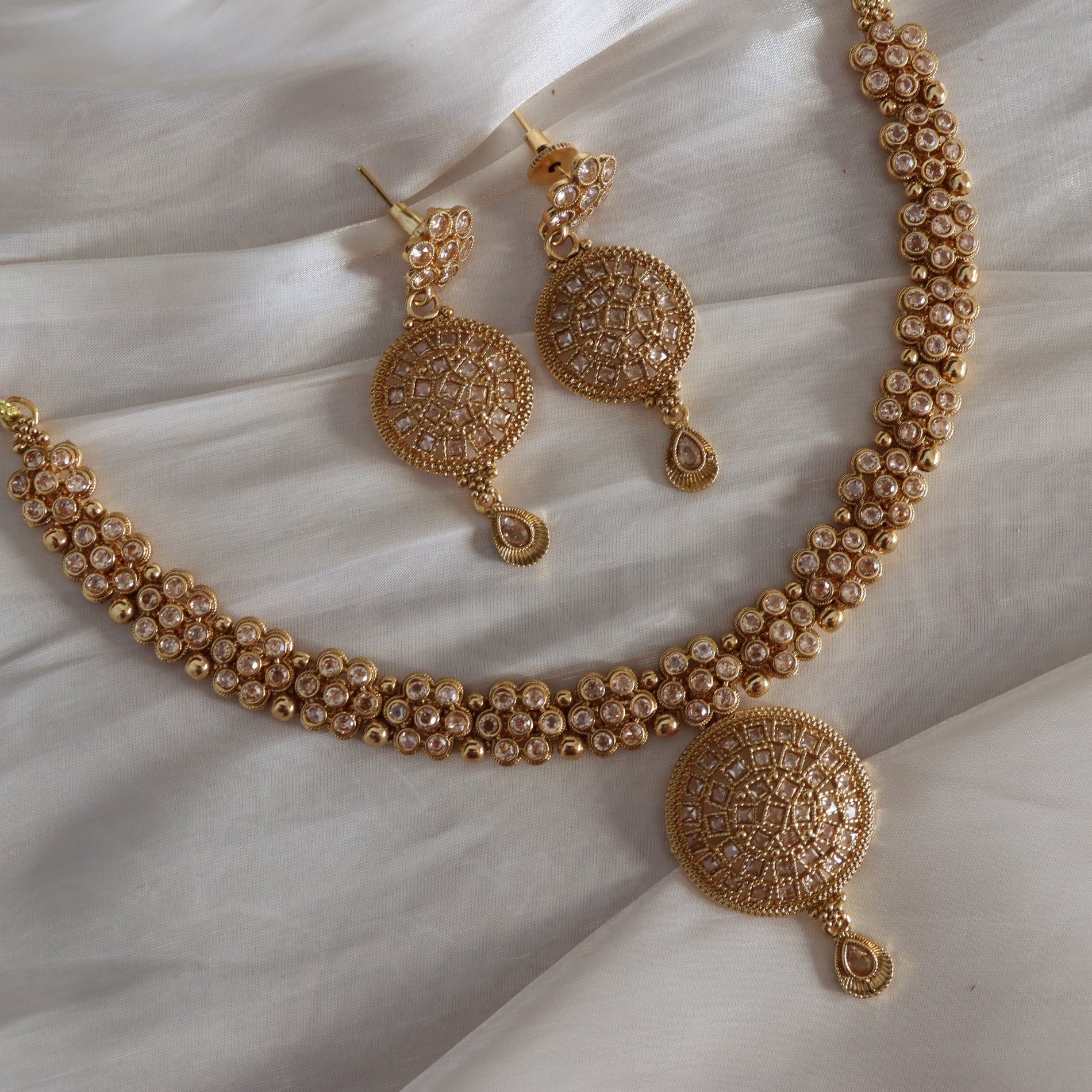 Gold necklace and earrings set on a textured white surface
