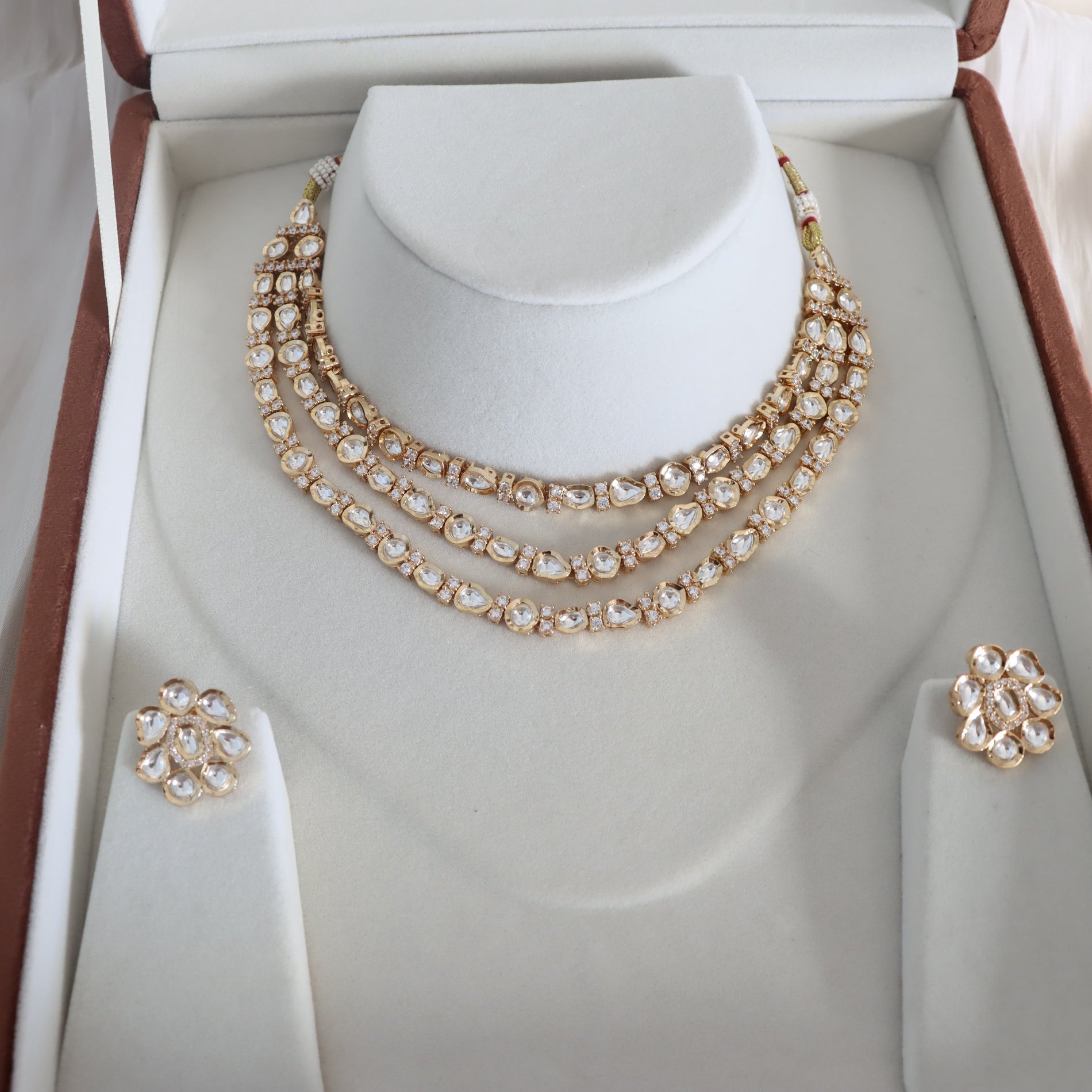 Gold necklace and earrings set on a mannequin bust in a jewelry box.