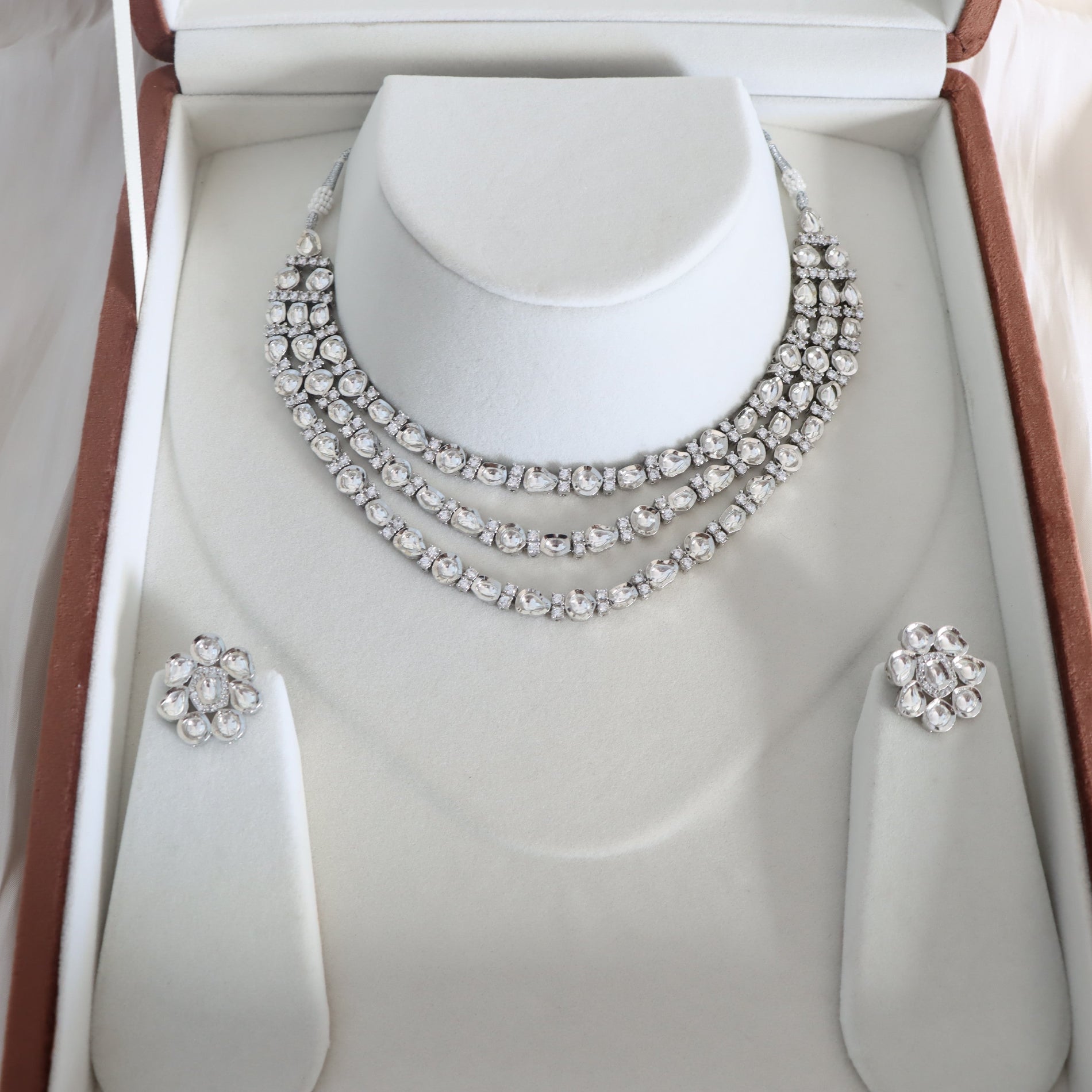 Silver necklace and earrings set on a mannequin bust in an open jewelry box.