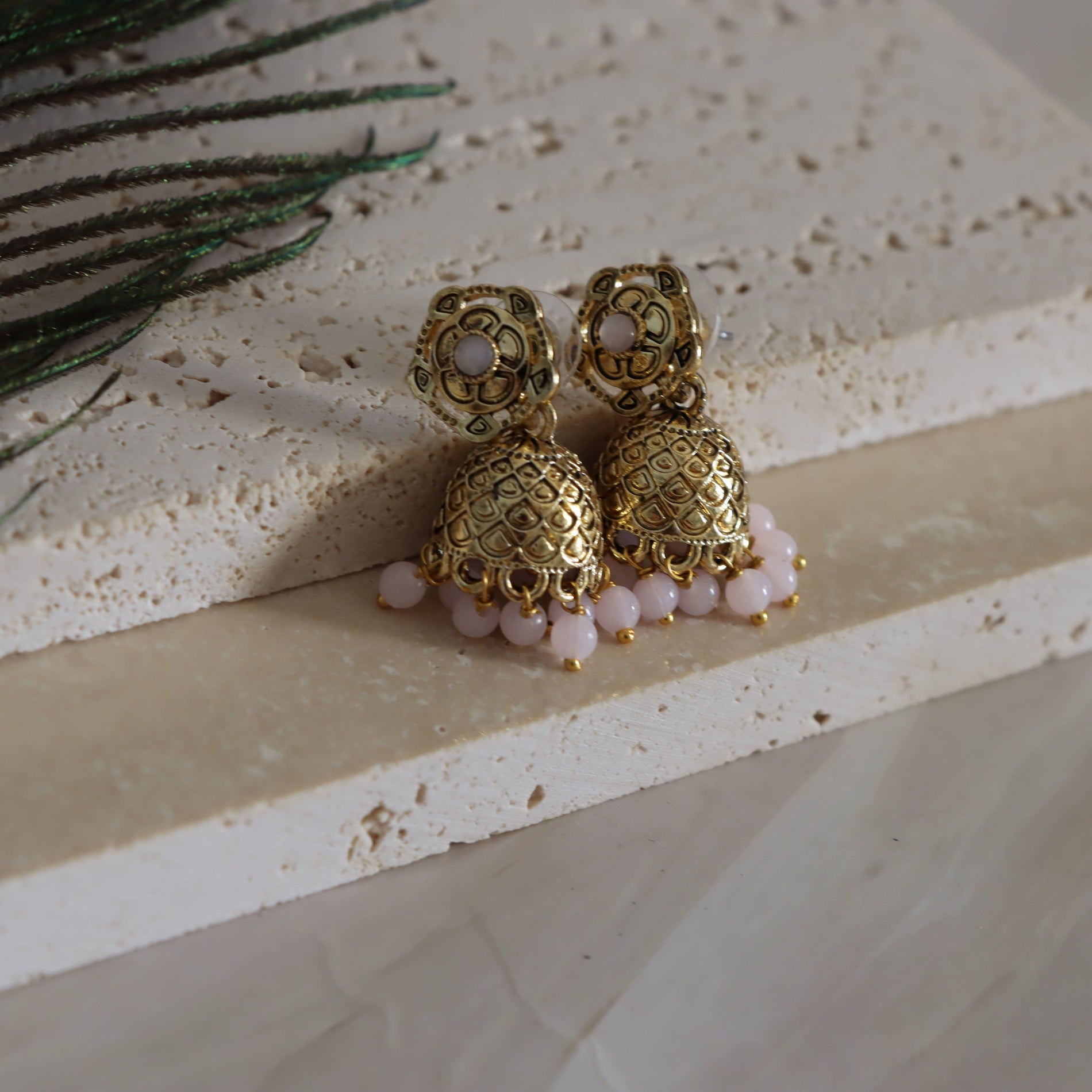 Gold earrings with pink beads on a textured surface
