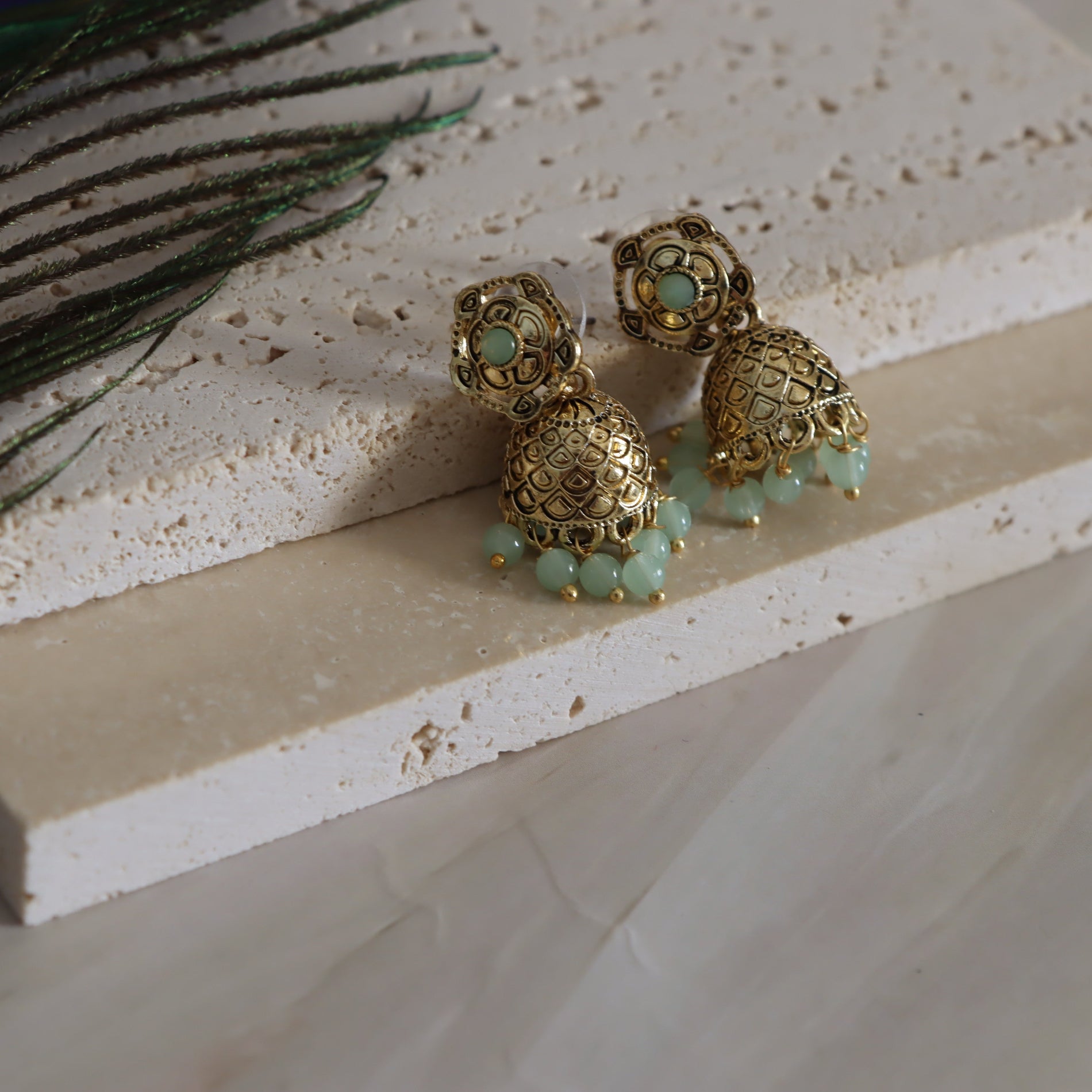 Gold earrings with green beads on a textured surface