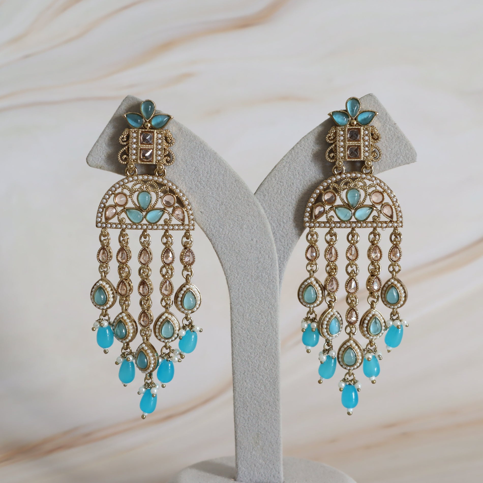Pair of turquoise and gold chandelier earrings on a white stand with a soft beige background