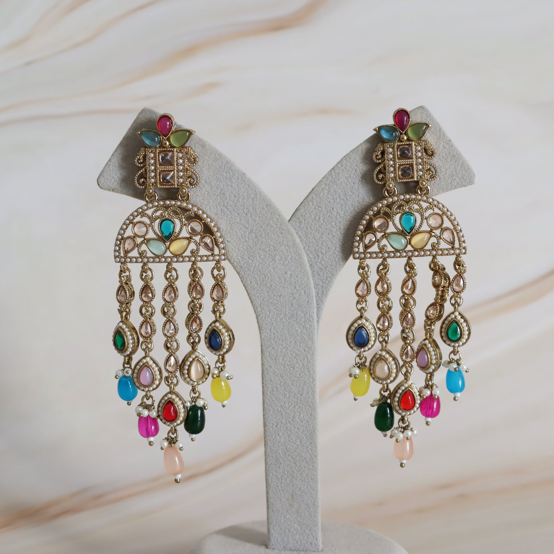 Pair of ornate earrings with colorful gemstones on a white stand.