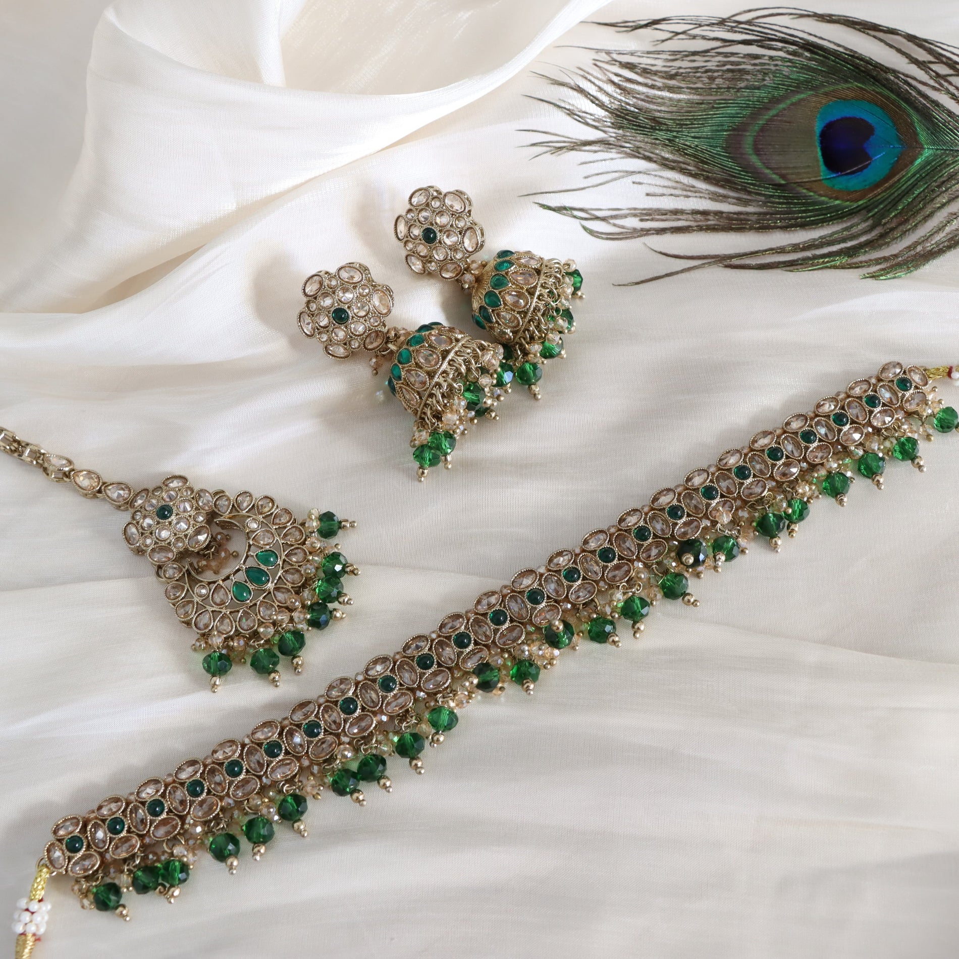 Jewelry set with necklace and earrings on a white fabric background with a peacock feather.