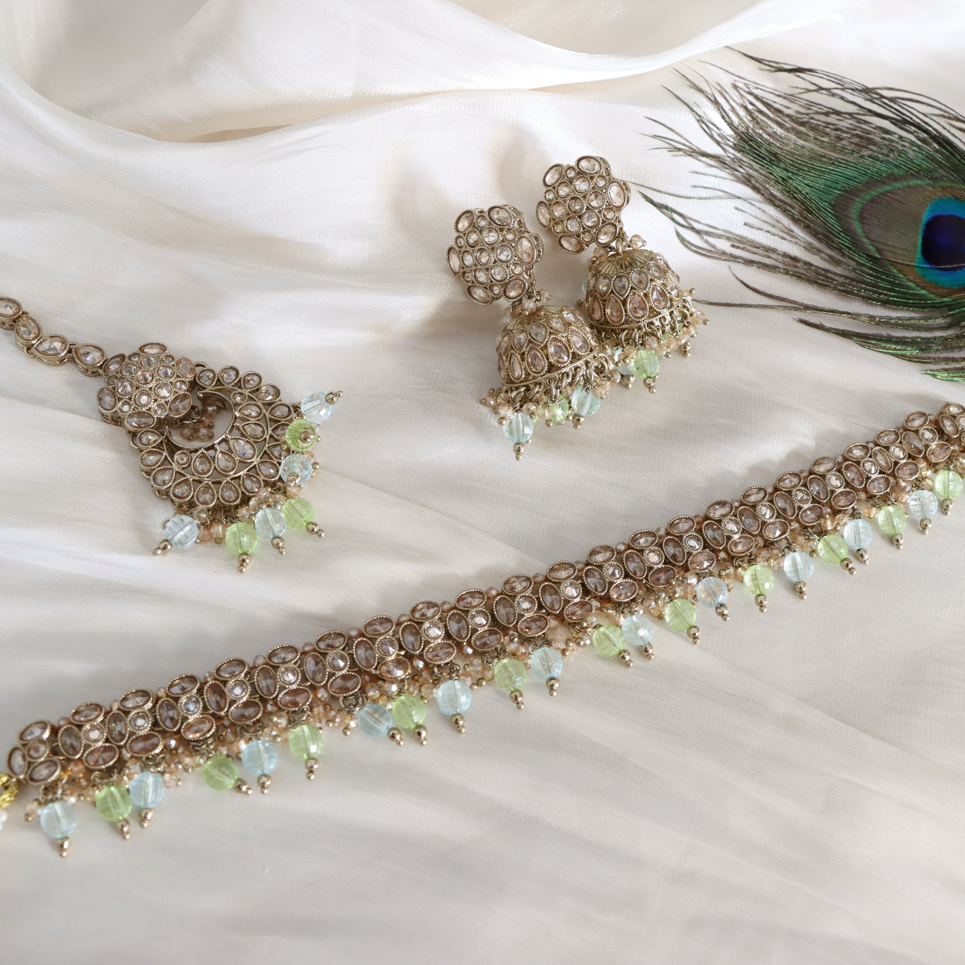 Jewelry set with necklace, earrings, and peacock feather on a white fabric background
