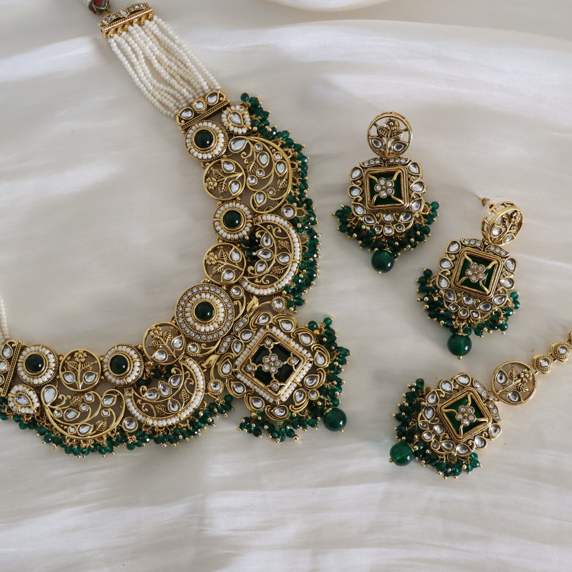 Ornate gold and green jewelry set on a white fabric background