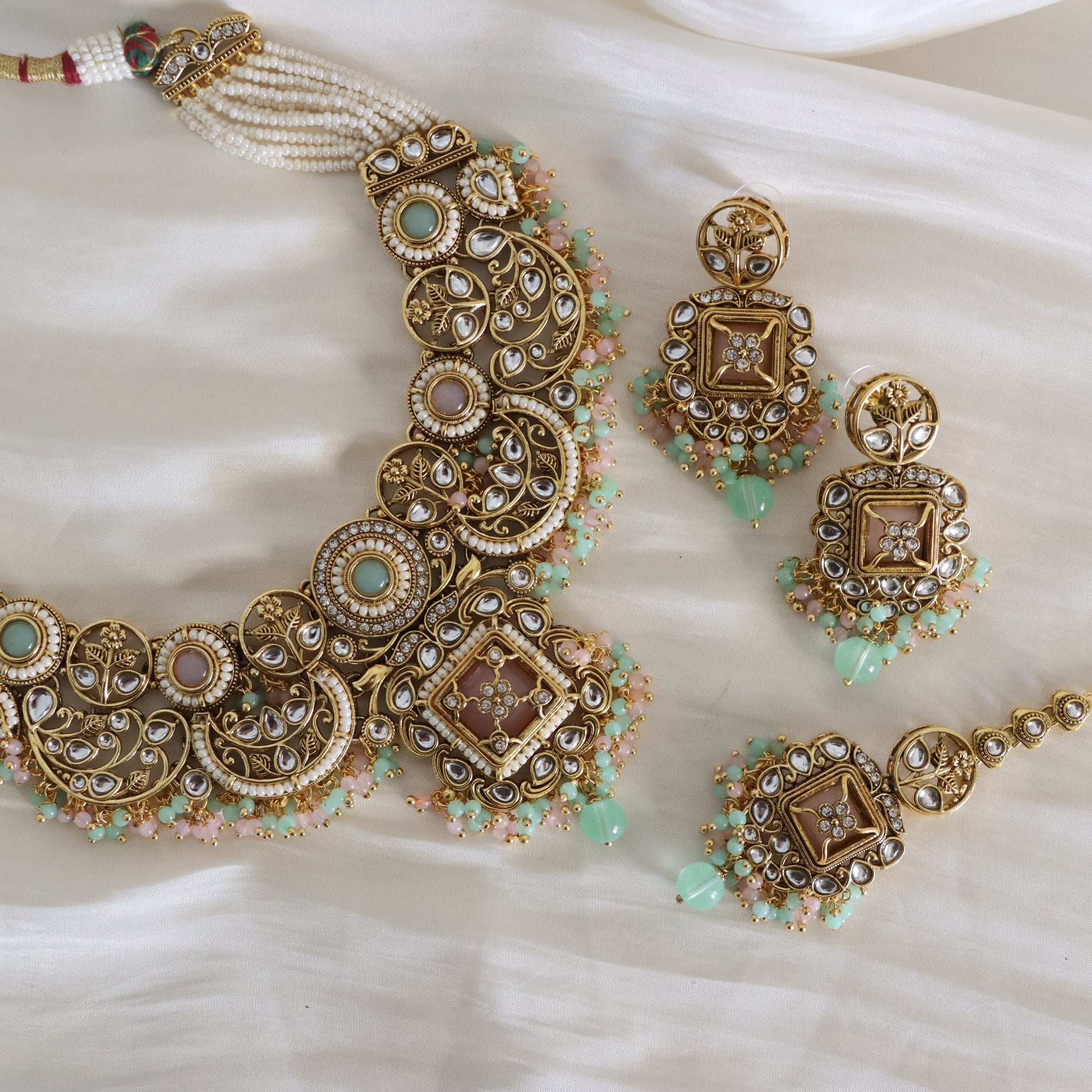 Ornate gold necklace and earrings with green gemstones on a white fabric background