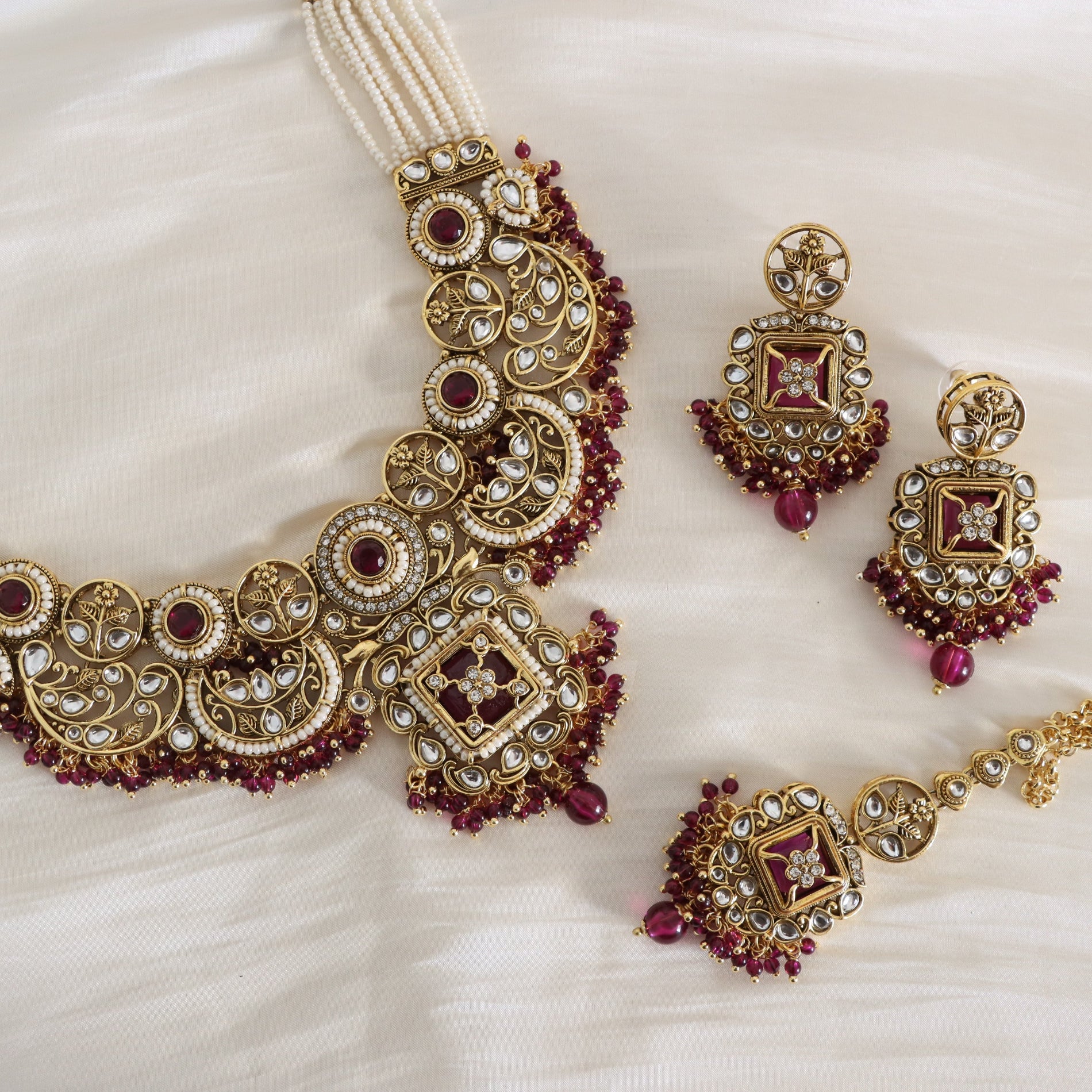 Ornate gold and red gemstone necklace with matching earrings on a white fabric background