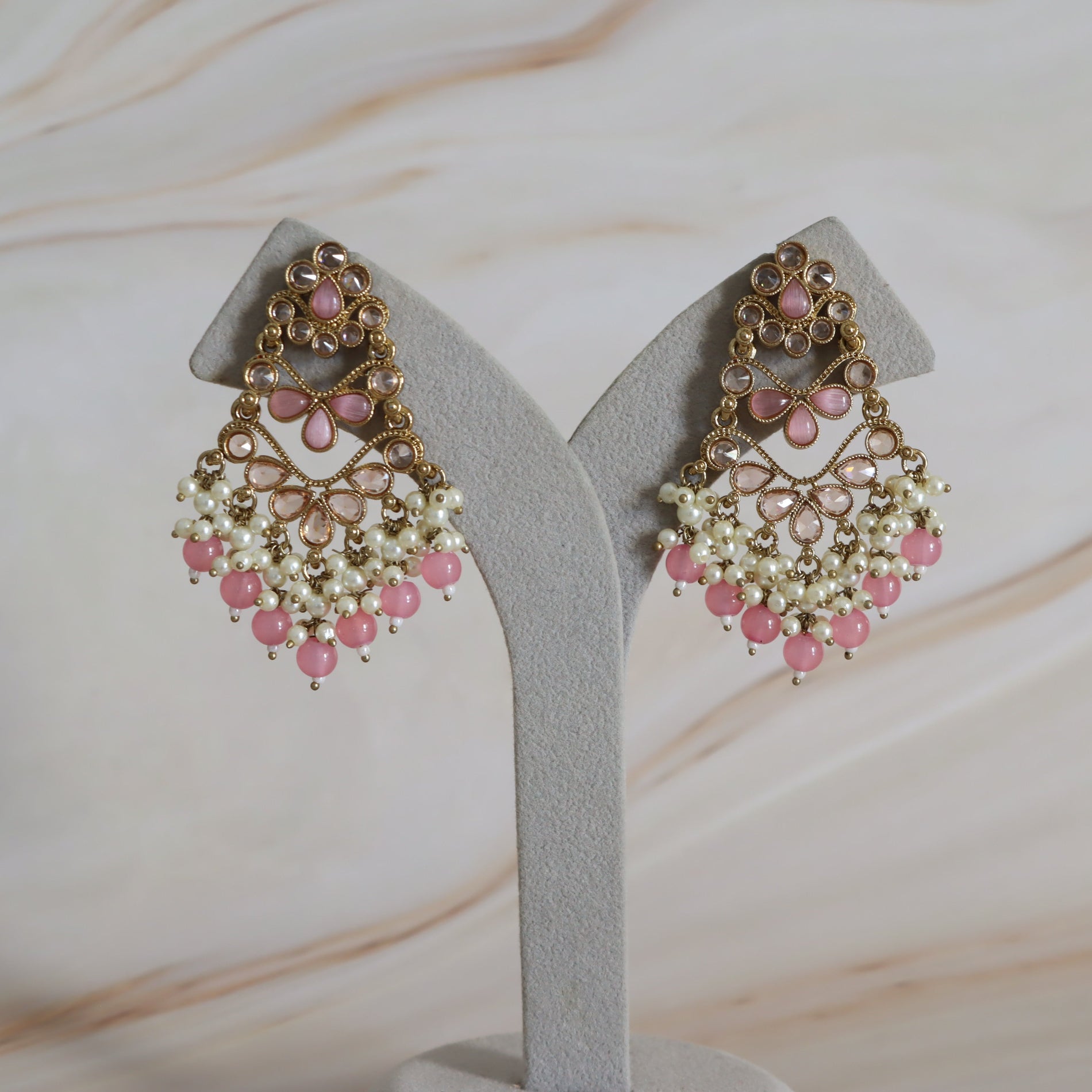 Pair of pink and gold earrings on a gray stand with a marble background