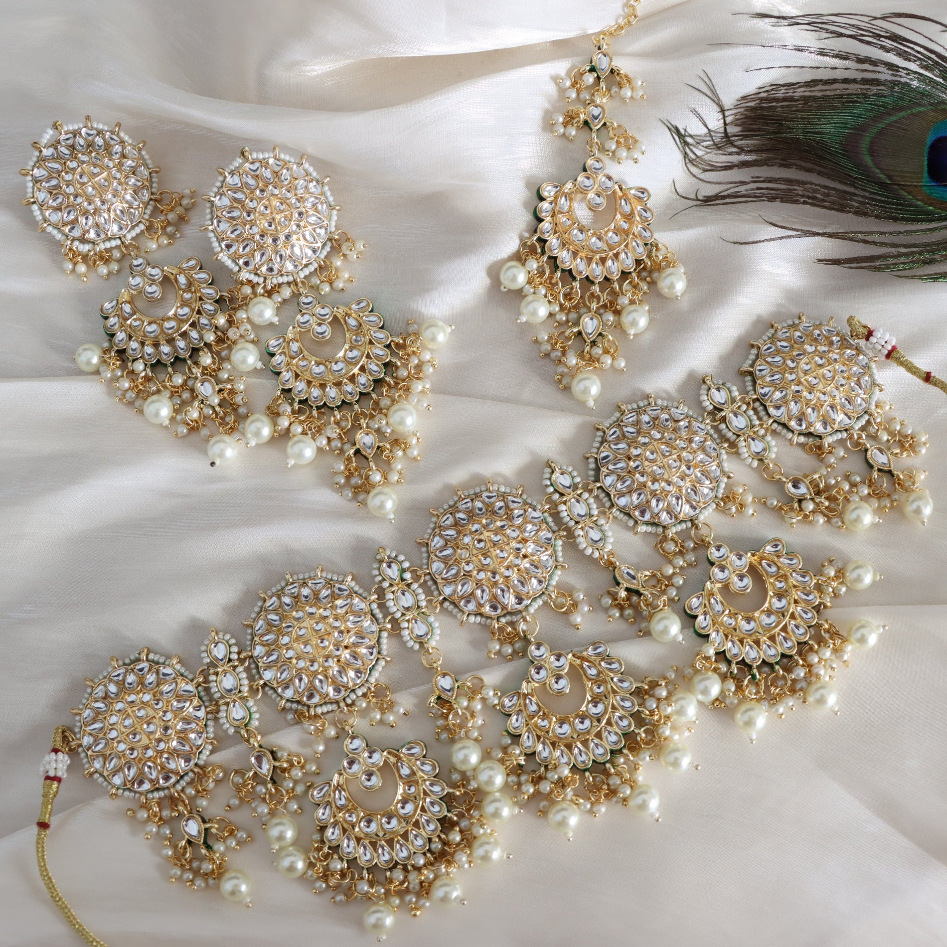 Gold and pearl jewelry set on a white fabric background with a peacock feather.