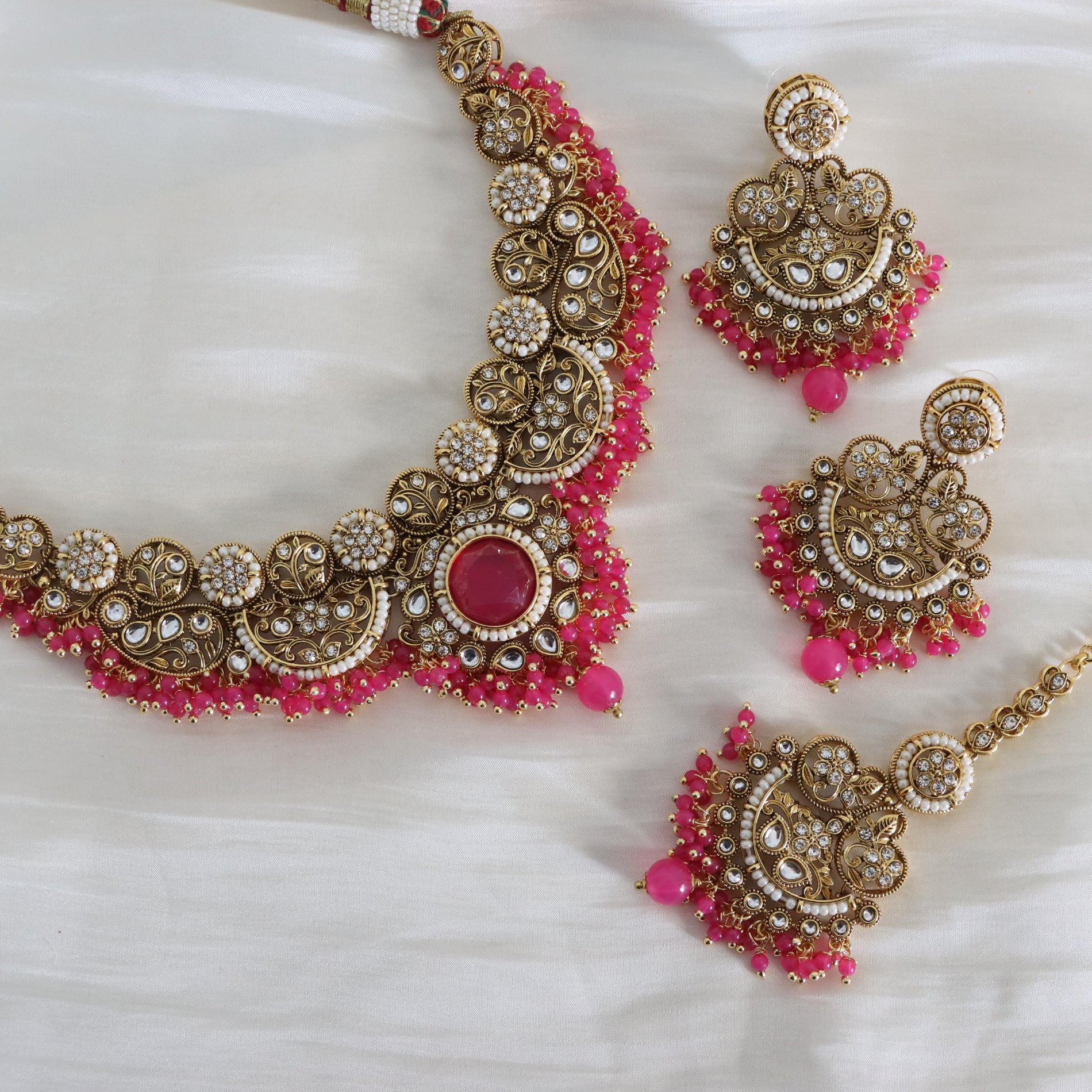 Ornate gold and pink jewelry set on a white fabric background