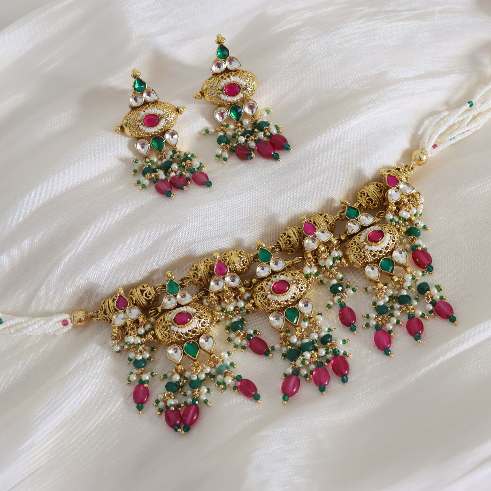 Ornate gold jewelry set with red and green stones on a white fabric background