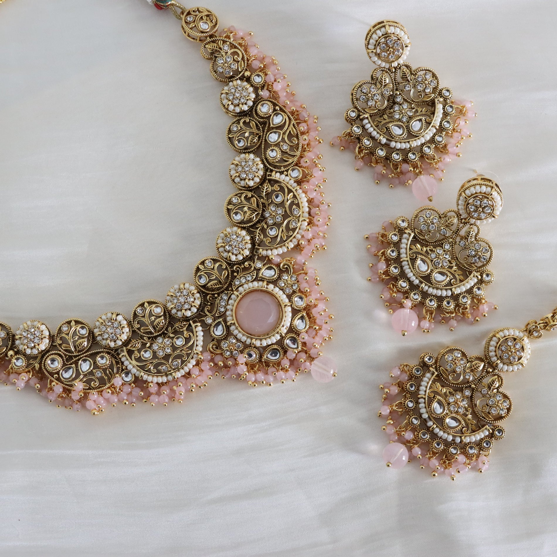 Ornate gold and pink jewelry set on a white background