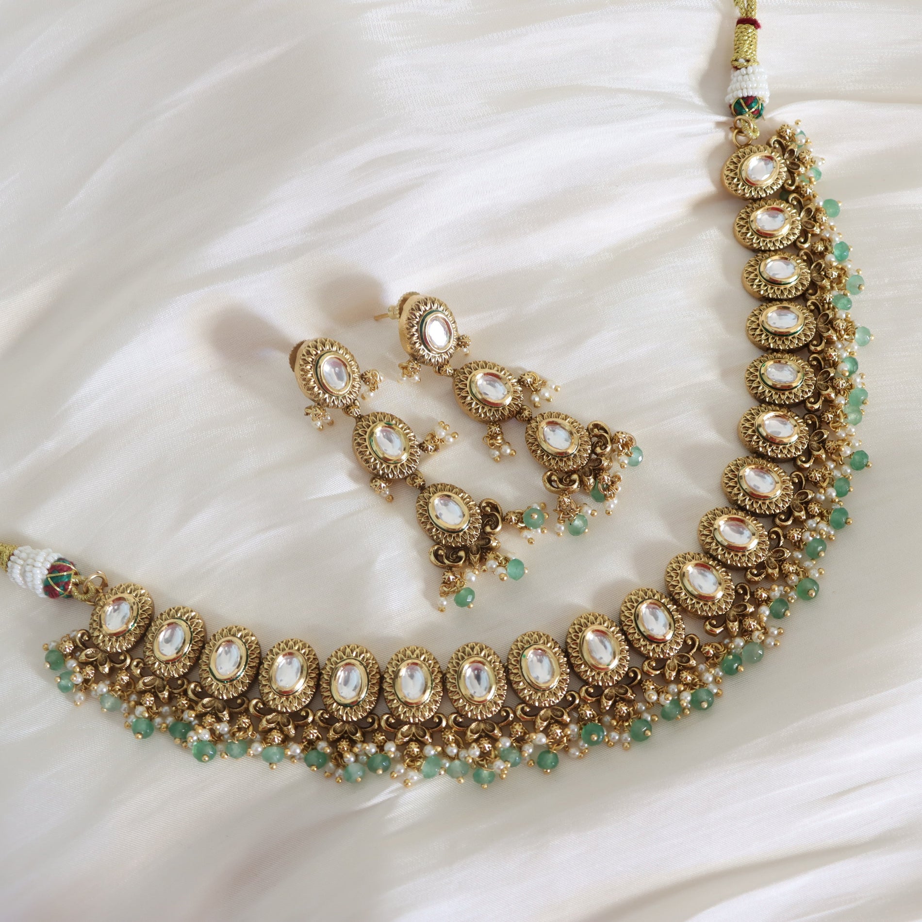 Ornate gold necklace with emerald green stones on a white fabric background